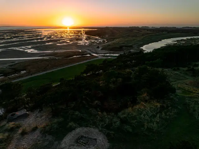 Aerial of tidal salt marshes and wooded dunes glowing at sunset