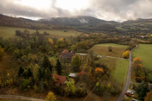 Aerial of an autumn valley with a hamlet and forested hills under low cloud