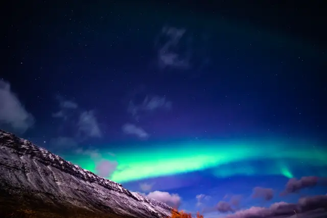 Green aurora borealis arcing over a snow-covered mountain under a starry sky