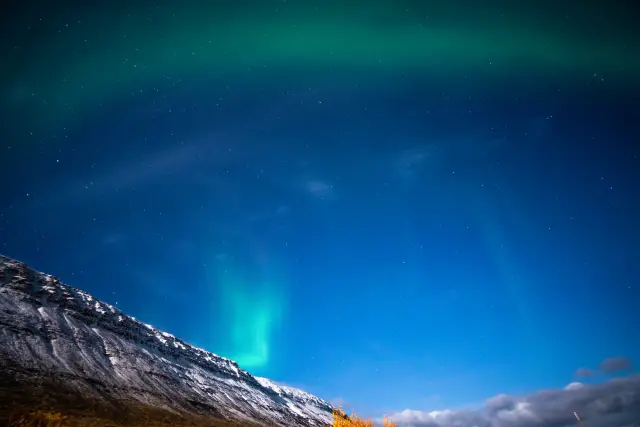 Green aurora borealis glowing above a snow-covered mountain ridge under a starry sky.
