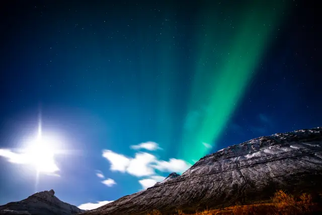 Green aurora and a bright moon above snow-dusted mountains, Iceland