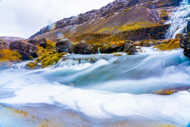 Long-exposure of a waterfall and river rushing over snow and mossy rocks, Iceland