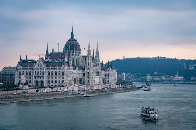 The Hungarian Parliament Building beside the Danube with a passing boat at dusk.