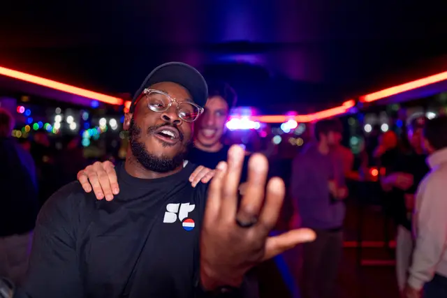 A man gesturing cheerfully at a lively event.