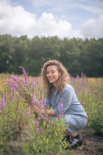 A woman crouching among wildflowers in a meadow.