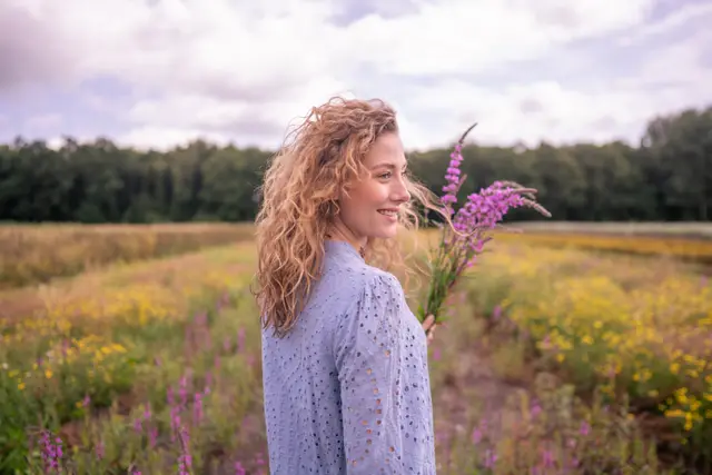 A woman in lilac holding wildflowers in a field.