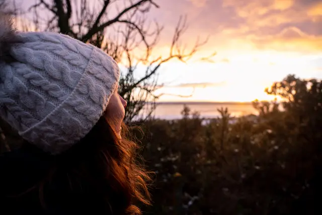 A person in a knitted hat watching the sunset over the sea.