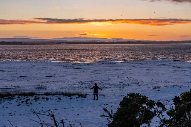 A lone figure on a vast snowy beach at sunset.
